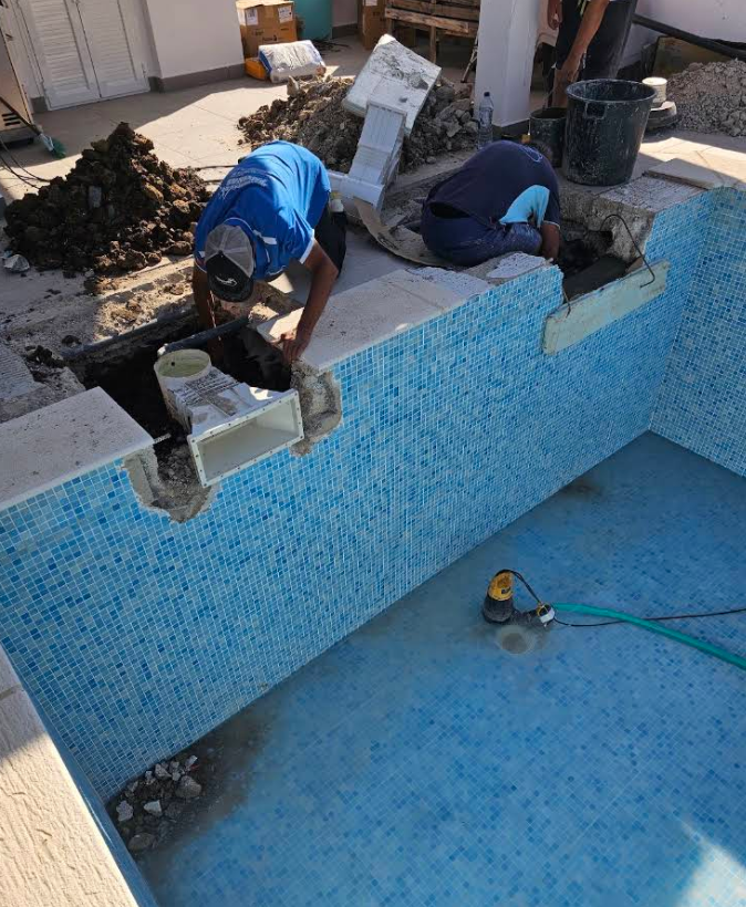 Trabalhadores a reparar a estrutura e skimmer de uma piscina